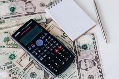 A calculator and a notepad on a stack of cash.