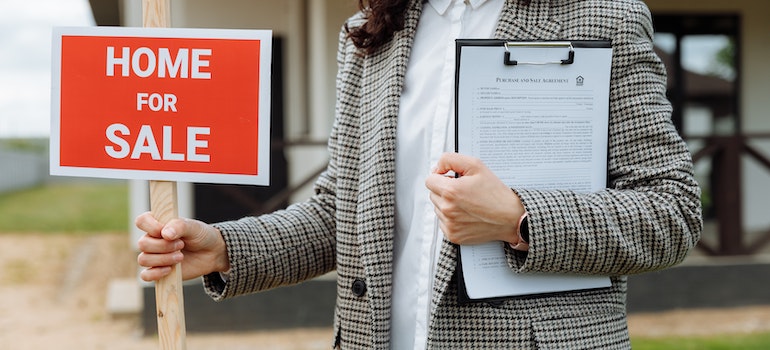 a real estate agent holding home for sale sign