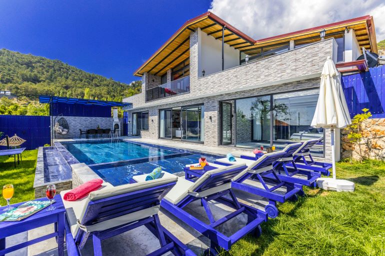 Seaside villa surrounded by lush gardens and mountain backdrop, highlighting Mediterranean beauty in locations attracting ultra-luxury property investors.