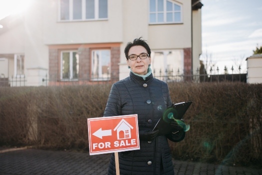 a woman standing in front of a house next to a home for sale sign